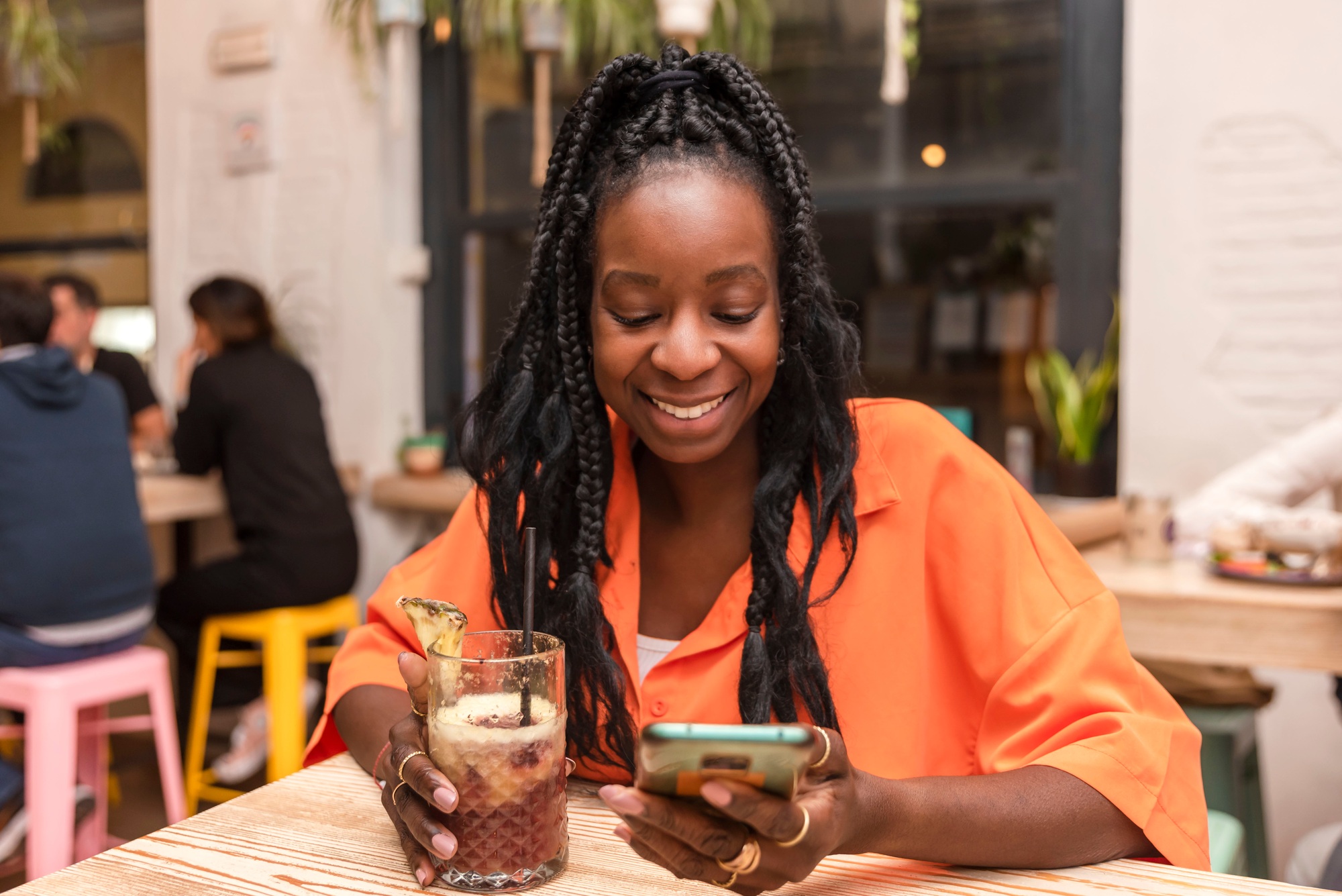 Happy african american woman using smart phone while relaxing having a drink in the bar